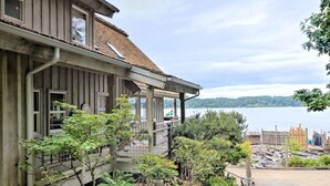 Une maison en bois dotée d’un balcon donnant sur un lac, entourée de verdure.