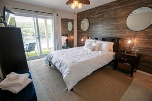 Een slaapkamer met een groot bed, een houten accentmuur, een ronde spiegel en uitzicht op een balkon.