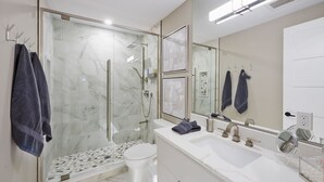 Ein modernes Badezimmer mit einer gläsernen Duschkabine, einer weißen Toilette und einem großen Spiegel über dem Waschbecken.