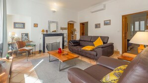 A living room with a brown sofa, a wooden coffee table, and a fireplace. There is a dining area with a table and chairs, and a kitchen area with a stove and cabinets. - Le Napoléon - Appt à moins d'un km de la plage (L'Île-Rousse)