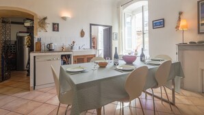 A dining area with a table set for four, a kitchen in the background, and a view of the outdoors. - Le Napoléon - Appt à moins d'un km de la plage (L'Île-Rousse)