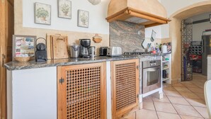 A kitchen with wooden cabinets, a granite countertop, and various appliances including a stove, oven, and coffee maker. - Le Napoléon - Appt à moins d'un km de la plage (L'Île-Rousse)