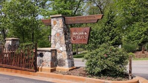 A sign for "Tan-Tara Estates" with a stone pillar and a wooden signboard, surrounded by greenery and a metal fence.