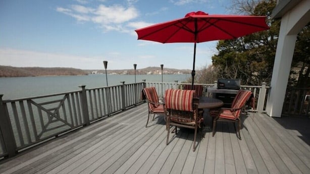 A deck with a table and chairs, a red umbrella, and a view of a lake.