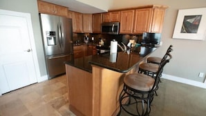 A kitchen with wooden cabinets, a stainless steel refrigerator, a microwave, and a bar stool.