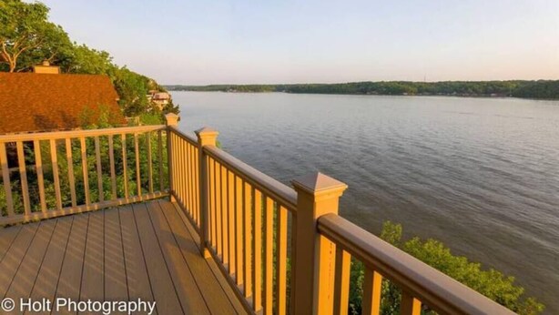 A wooden deck with a railing overlooking a calm river. - Stunning Lake View 4br 5ba (Osage Beach)