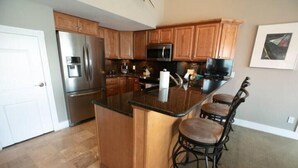 A kitchen with wooden cabinets, a stainless steel refrigerator, a microwave, and a bar stool. - Stunning Lake View 4br 5ba (Osage Beach)
