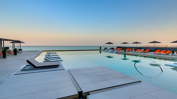 Ein Poolbereich mit Liegestühlen und Sonnenschirmen mit Blick auf ein ruhiges Meer.