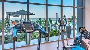 Ein Fitnessraum mit Trainingsgeräten und Meerblick durch große Fenster.