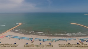 Eine Luftaufnahme eines Strandes mit Reihen blauer Sonnenschirme und einem Sandufer.