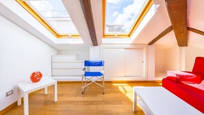 Un apartamento tipo loft moderno con tragaluces, un sofá rojo y una silla plegable azul.