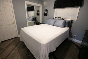 A bedroom with a bed, a door, a mirror, and a window with a black valance.