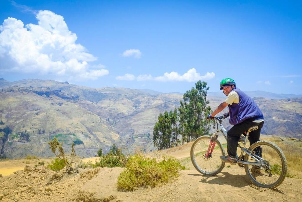Una persona montando una bicicleta de montaña por un sendero de tierra, con un paisaje montañoso al fondo.