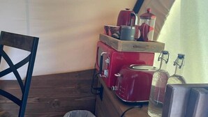 Une petite cuisine équipée avec une machine à café rouge, une bouilloire et une cafetière, le tout posé sur une étagère en bois.