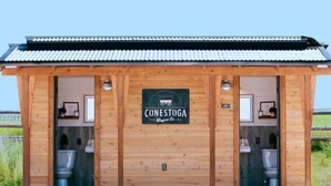 Eine Holzhütte mit einem Schild, das "CONESTOGA Wagon Co." zeigt, und zwei sichtbaren Toiletten.
