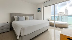 A modern bedroom with a large bed, a nightstand, and a view of the sea through a sliding glass door. - 16th Floor Infinitum 1 Bedroom Apt (Cartagena)