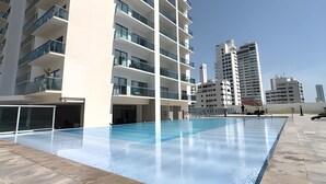 A modern building with a swimming pool, multiple balconies, and a clear sky. - 16th Floor Infinitum 1 Bedroom Apt (Cartagena)