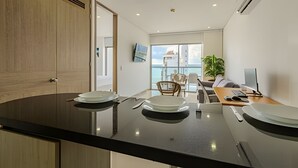 A modern kitchen with a large island, a dining area with a view of the sea, and a living area with a sofa and a desk. - 16th Floor Infinitum 1 Bedroom Apt (Cartagena)
