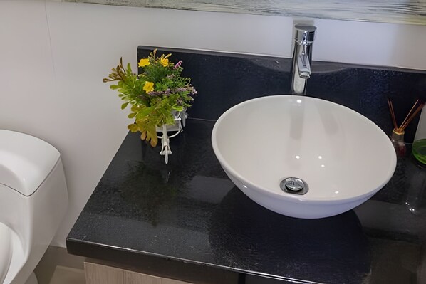 A bathroom with a white sink, a black countertop, and a small potted plant with yellow flowers.
