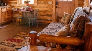 A cozy log cabin interior with a dining area, a sofa, and a table with a glass. - The Bighole Cabin at J&J Cabins (Salmon)