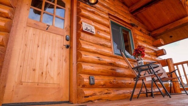 A wooden cabin with a number 7 door, a small window, and a table with chairs outside. - The Bighole Cabin at J&J Cabins (Salmon)
