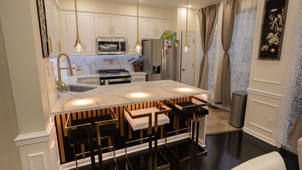 A modern kitchen with white cabinets, a central island with bar stools, stainless steel appliances, and pendant lighting. - Luxury Townhome Minutes From DC (Alexandria)