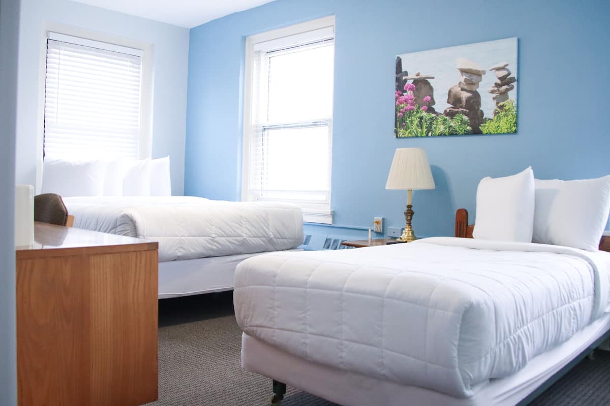 A hotel room with two beds, a wooden nightstand, a lamp, and a painting on the wall.