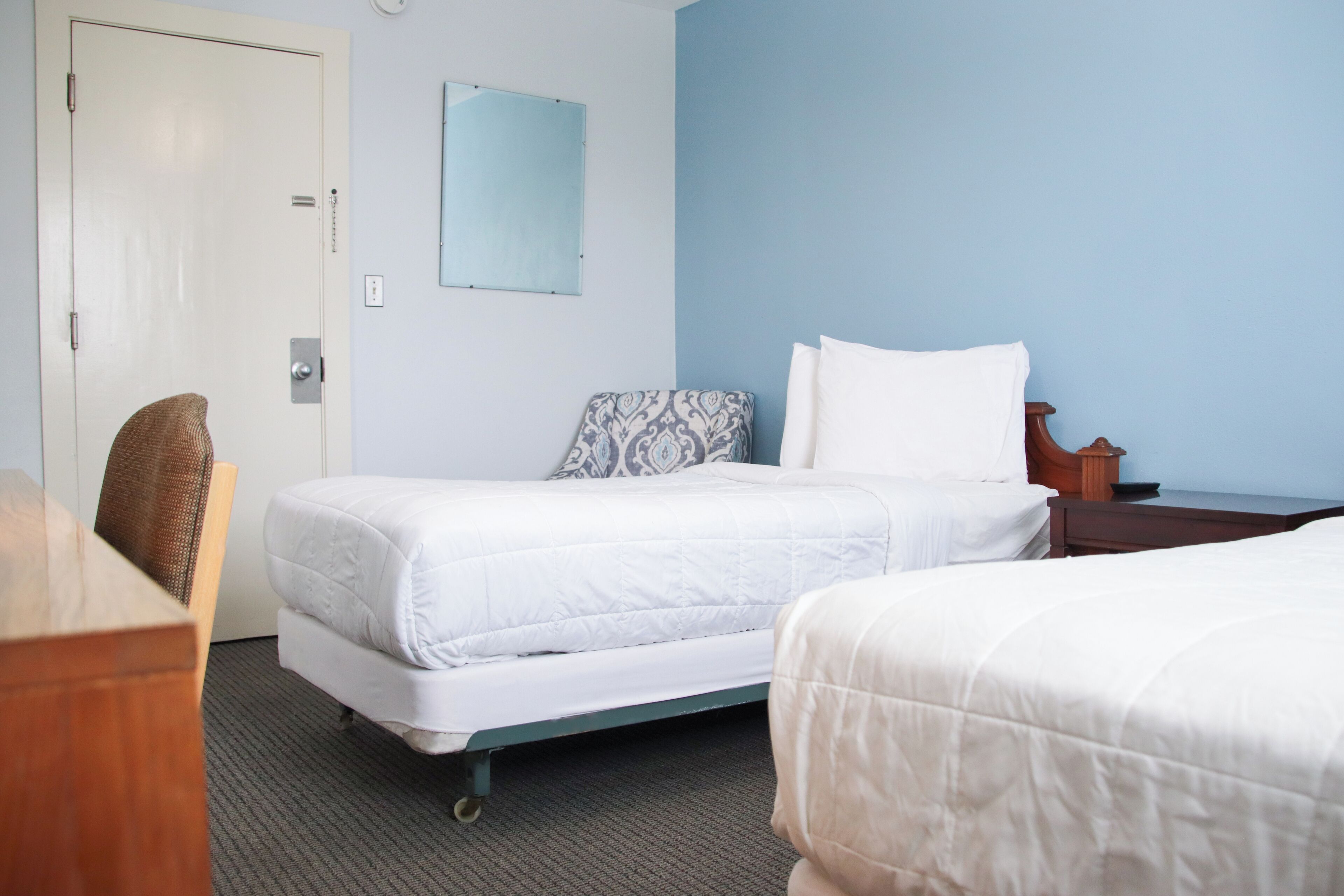 Une chambre d’hôtel avec deux lits, un bureau en bois, une chaise, un miroir et une porte.