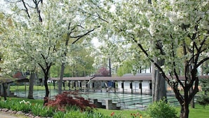 A row of covered picnic tables and a building with a sloped roof, surrounded by blooming trees and a well-maintained lawn. - The Fountain Inn (Marblehead)