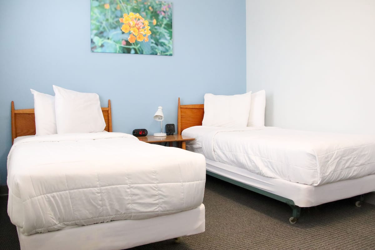 Two single beds with white bedding, a nightstand with a lamp, and a clock.