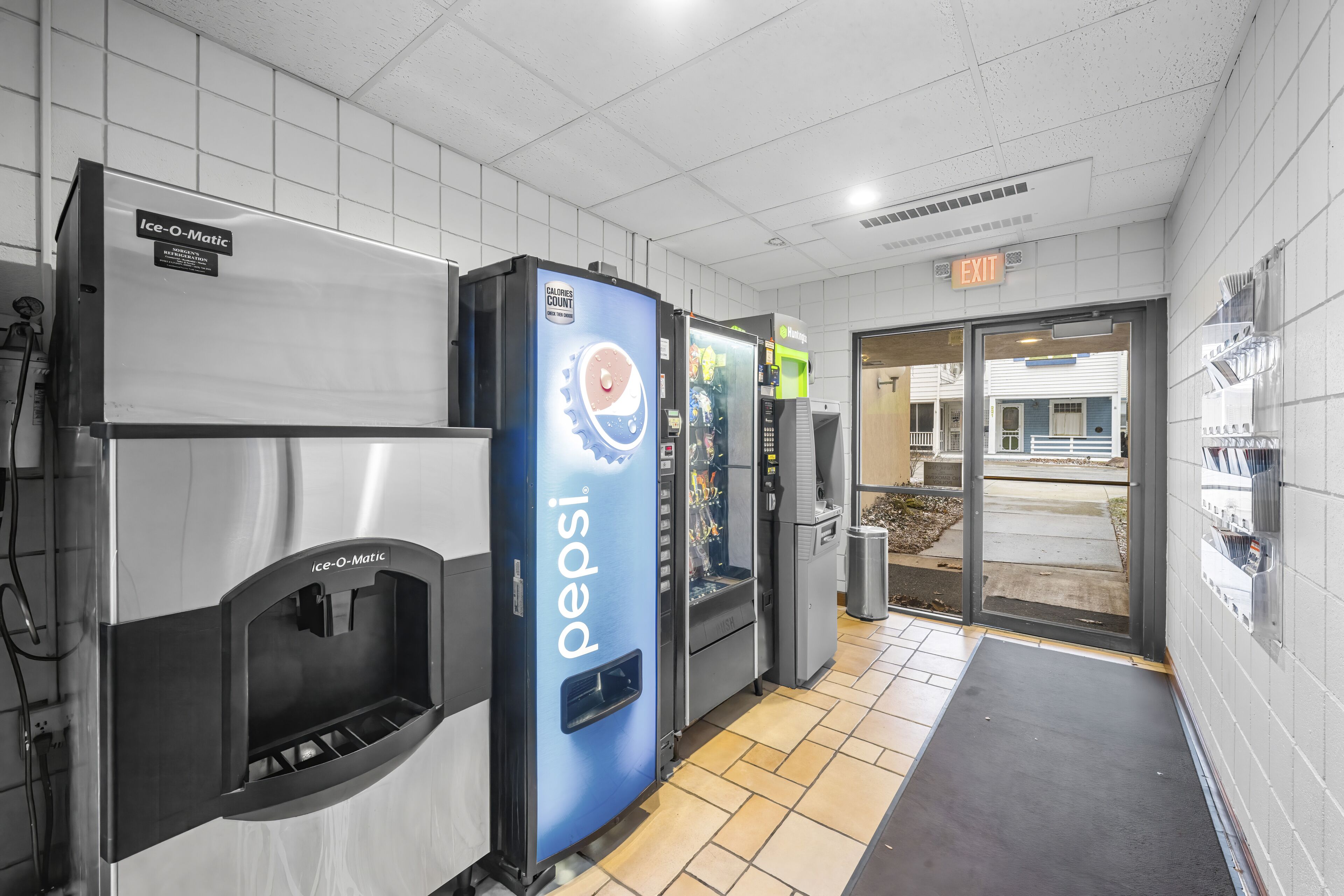 A clean, modern restroom with a Pepsi refrigerator, an Ice-O-Matic dispenser, and a clear exit sign.