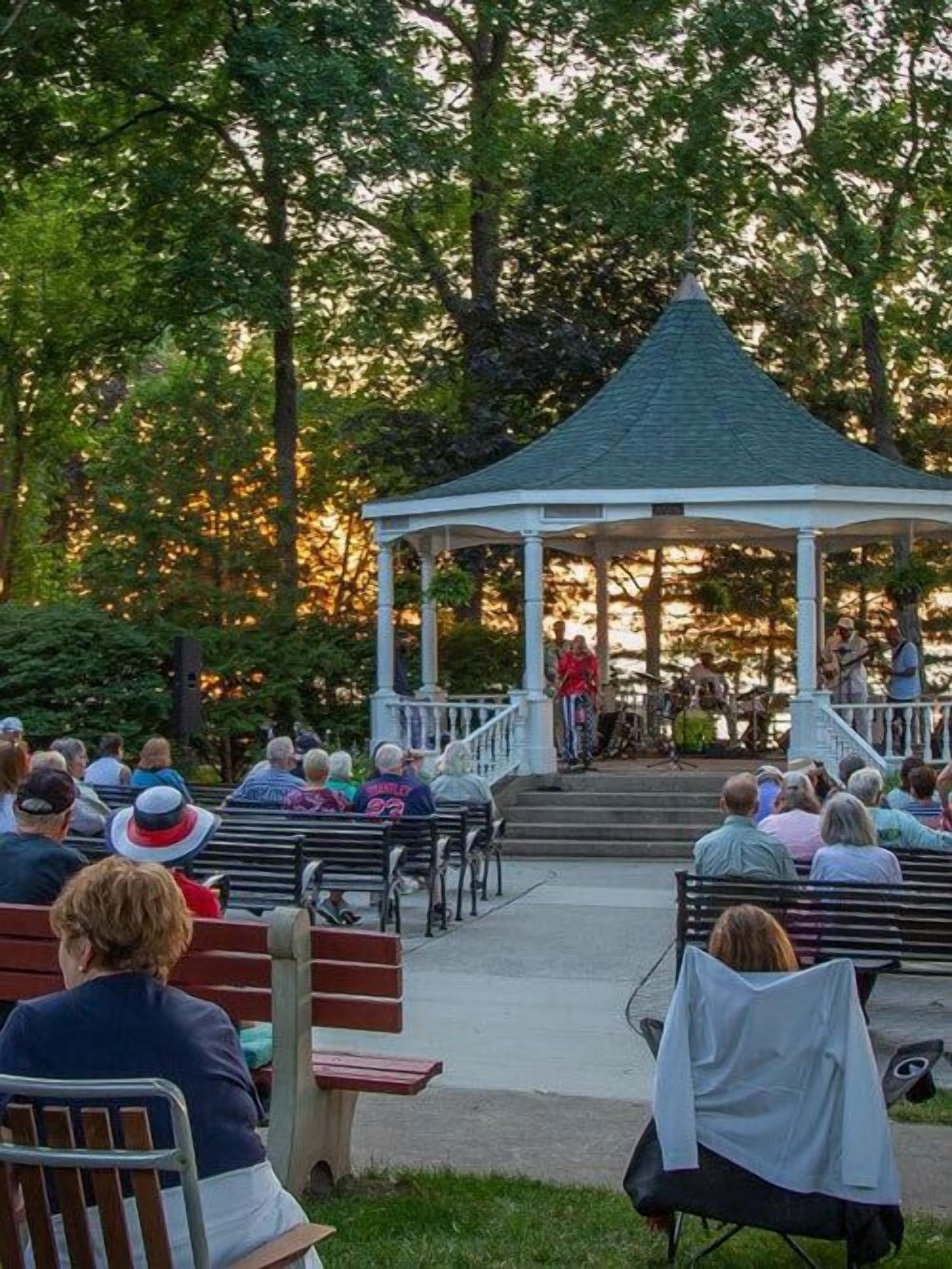 A gazebo with a group of people seated on benches around it, likely attending an event.