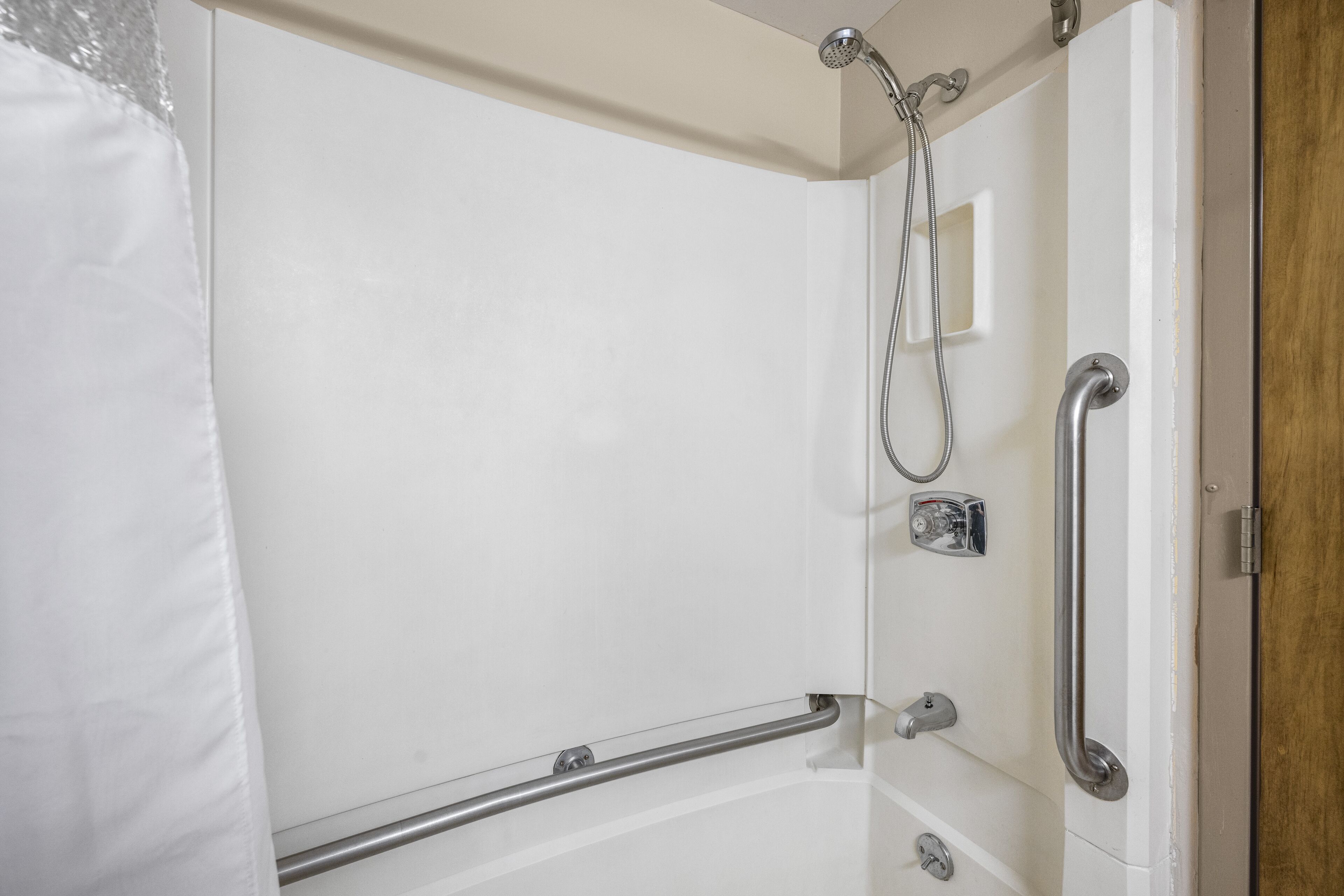A bathroom with a shower, grab bars, and a door with a wooden panel.