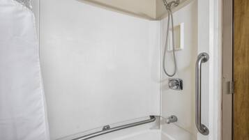 A bathroom with a shower, grab bars, and a door with a wooden panel.