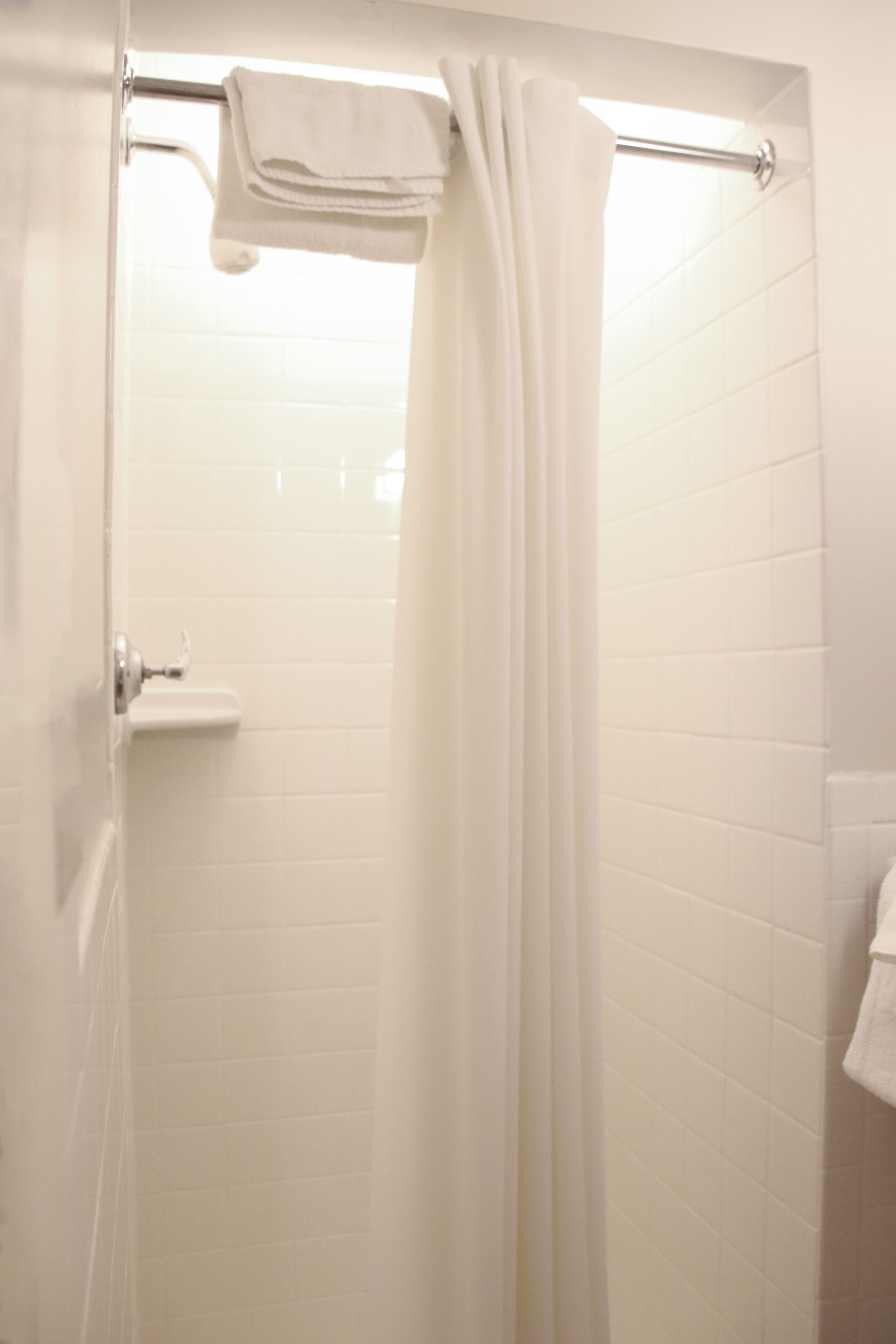 A bathroom with white tiled walls, a shower curtain, and a towel rack.