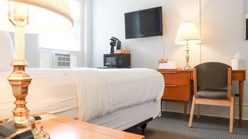 Quarto de hotel com cama, escrivaninha, cadeira, televisão e abajur.