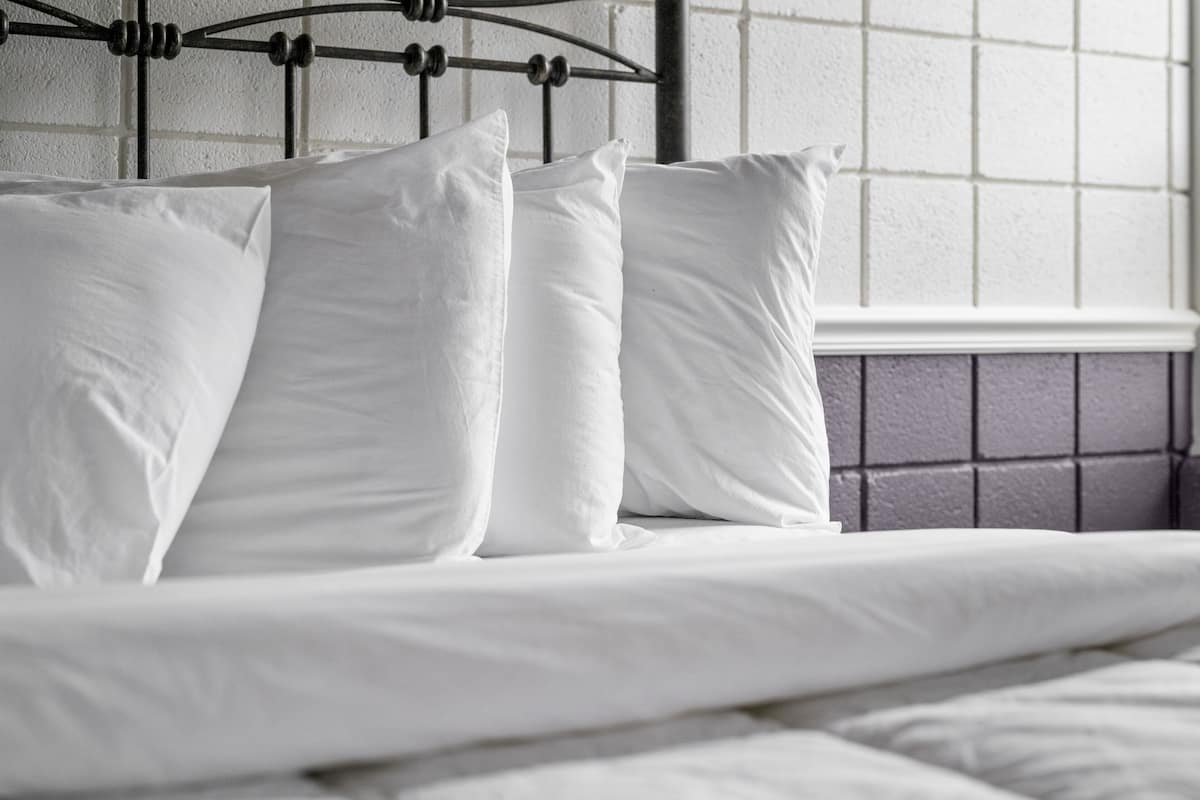 A bed with white bedding and pillows, a metal headboard, and a window with a grid pattern.