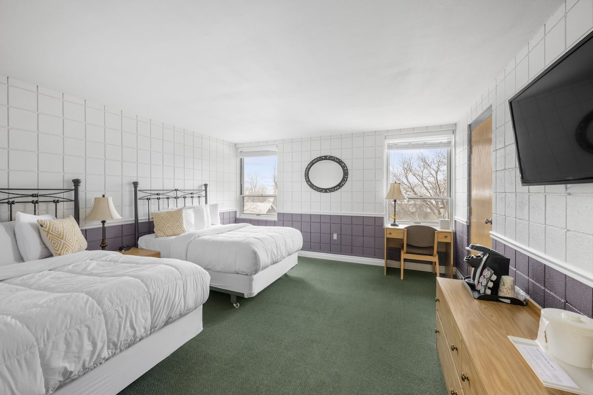A hotel room with two beds, a desk, a chair, a TV, and a window with a view of trees.