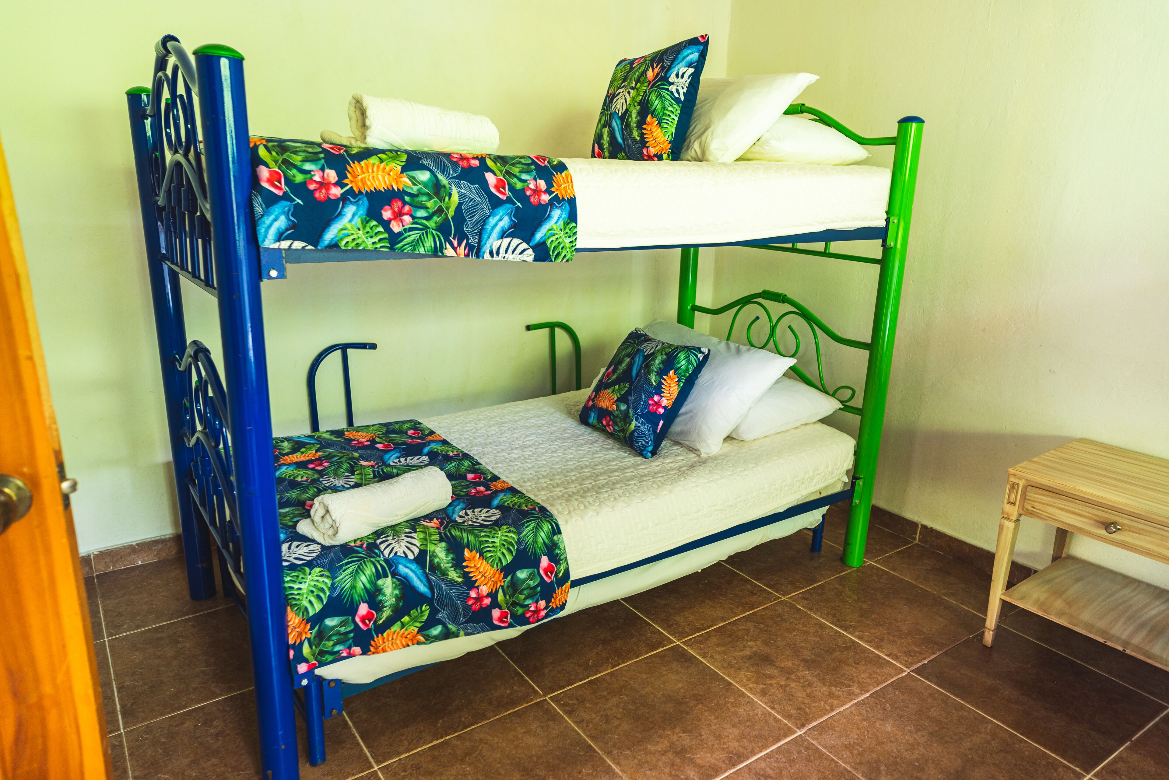 Una cama litera con una colcha estampada, una mesita de madera y un suelo de baldosas.