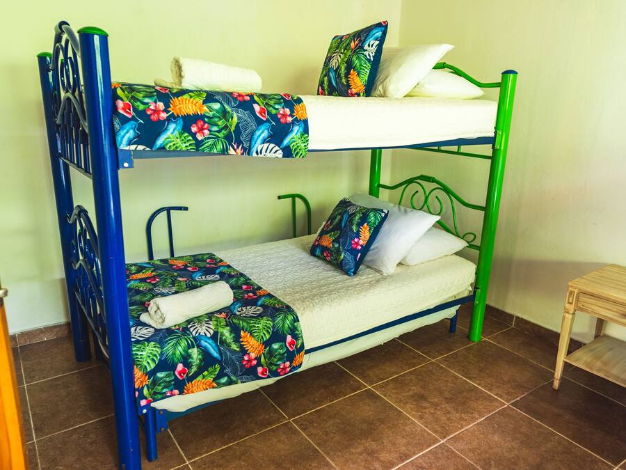 Una cama litera con una colcha estampada, una mesita de madera y un suelo de baldosas.