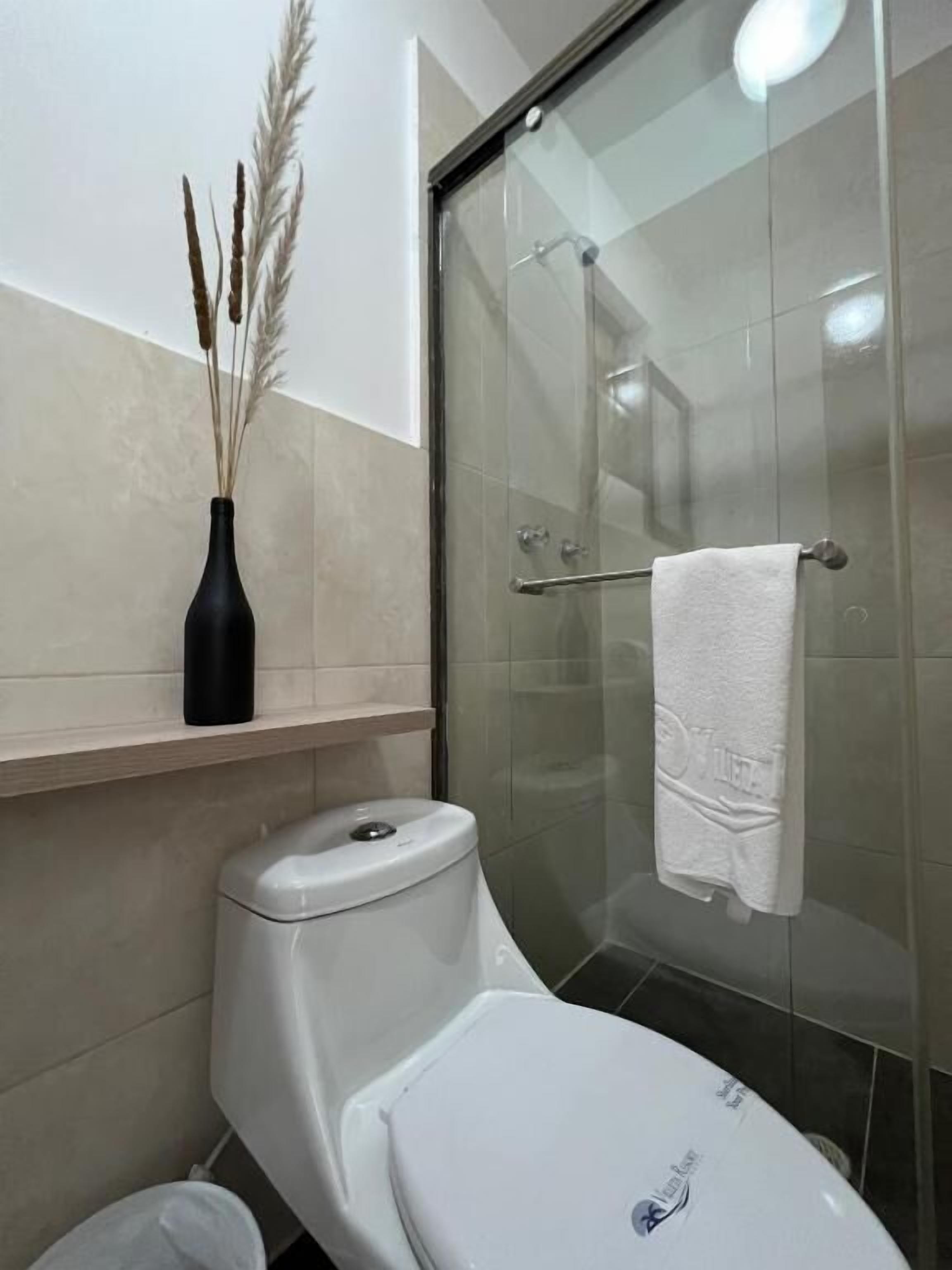 A bathroom with a toilet, a glass shower enclosure, and a shelf with a vase.