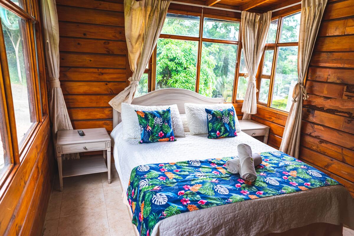 Een houten slaapkamer met een bed, nachtkastjes en grote ramen.