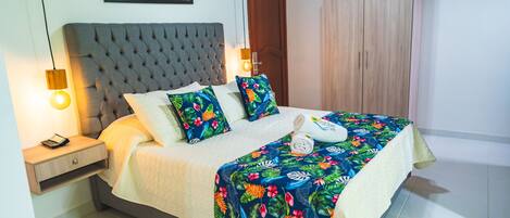 A neatly made bed with a floral bedspread, a bedside table with a lamp, and a wooden wardrobe.