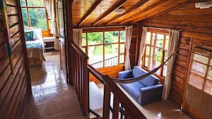 A wooden cabin interior with a staircase leading to a balcony, a blue sofa, and a bed with a colorful blanket. - Villeta Resort Hotel (Villeta)