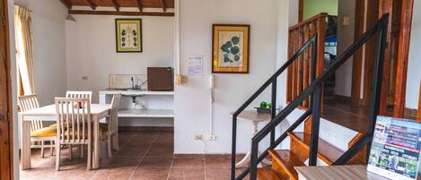 A dining area with wooden chairs and a table, a staircase with wooden railings, and a wall with framed botanical prints.