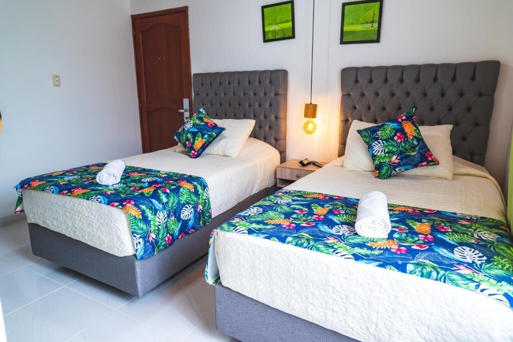 A hotel room with two beds, each with a floral bedspread and a white pillow. There is a wooden door and a wall-mounted light fixture.