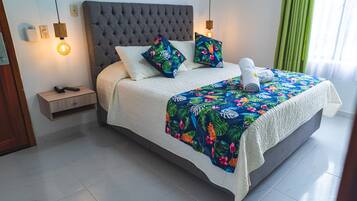 Un lit bien fait, recouvert d’une couvre-lit à motifs floraux, avec une tête de lit rembourrée de couleur grise et deux oreillers ornés de motifs tropicaux.