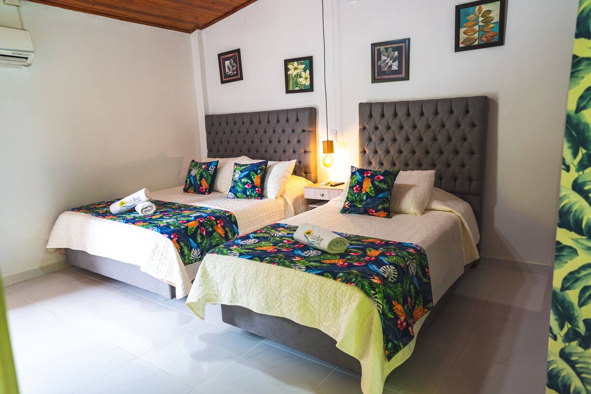 Een tweepersoonskamer met twee bedden, elk met een bloemenprint deken en een witte plaids. Tussen de bedden staat een nachtkastje met een lamp.