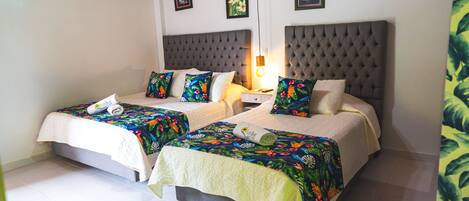 Une chambre double avec deux lits, chacun agrémenté d'une couvre-lit à motifs floraux et d'un plaid blanc. Une table de chevet avec une lampe se trouve entre les deux lits.