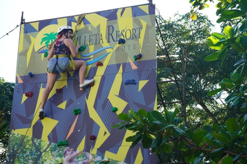 A rock climbing wall with a palm tree and hotel name at the top.